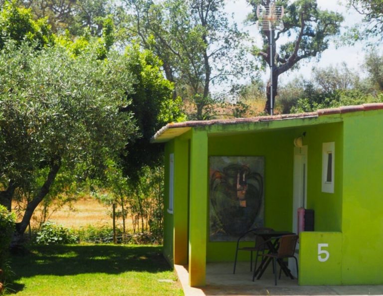 Eine leuchtend lindgrüne Hütte mit der Nummer 5 steht auf einer von Bäumen umgebenen Wiese, und durch den offenen Eingang sind Stühle zu sehen.