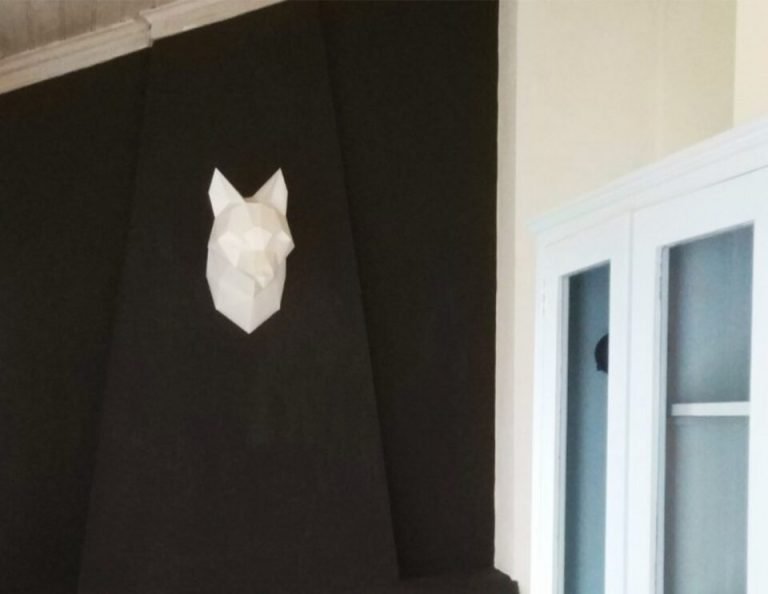 Ein minimalistisches, weißes, geometrisches Wolfskopfdesign auf einer schwarzen Akzentwand über einem Kamin mit freiliegendem Ziegelinterieur.