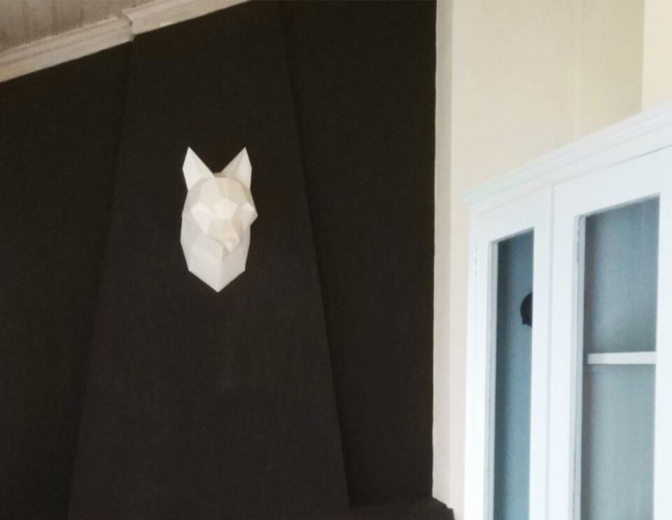 Ein minimalistisches, weißes, geometrisches Wolfskopfdesign auf einer schwarzen Akzentwand über einem Kamin mit freiliegendem Ziegelinterieur.