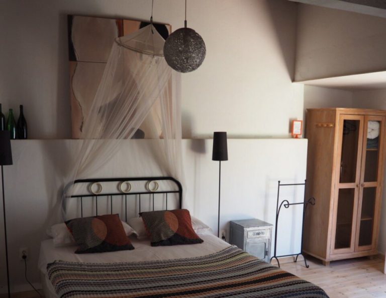Ein modernes Schlafzimmer mit einem schwarzen Eisenbett mit weißem Baldachin, gestreifter Bettwäsche in Erdtönen, dekorativen Kissen, einem Holzschrank, Hängeleuchten und minimalistischen Möbeln auf hellem Holzboden.