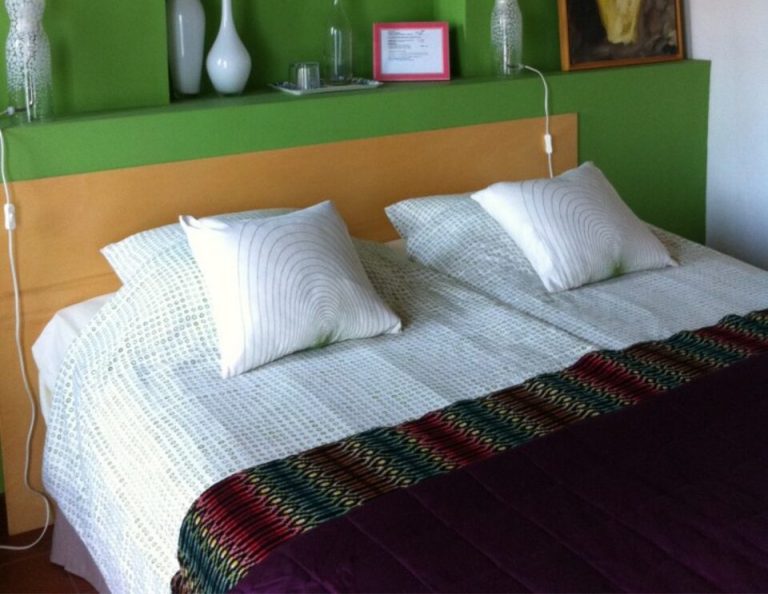Ein modernes Schlafzimmer mit einem Holzbettgestell und weißen Kissen vor einer leuchtend grünen Wand mit eingebauten Regalen und dekorativen Vasen und Kunstwerken über dem Kopfteil.