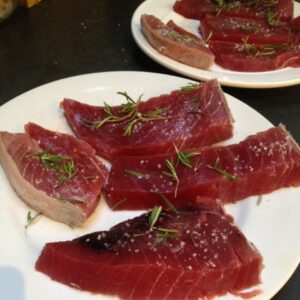 Fatias de atum cru decoradas com alecrim fresco e sal grosso em pratos brancos
