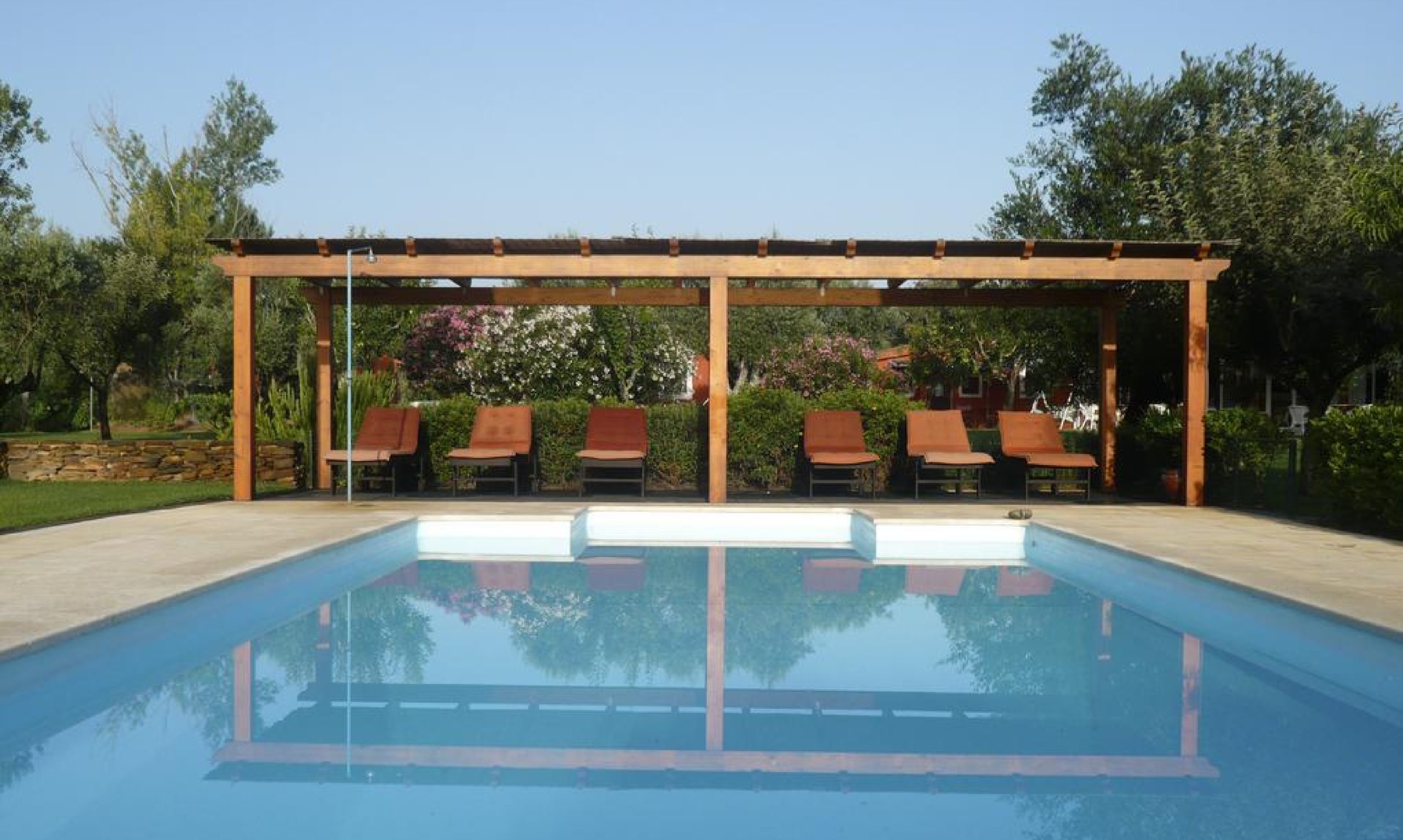 Piscina al aire libre con pérgola de madera, tumbonas y un exuberante jardín a su alrededor