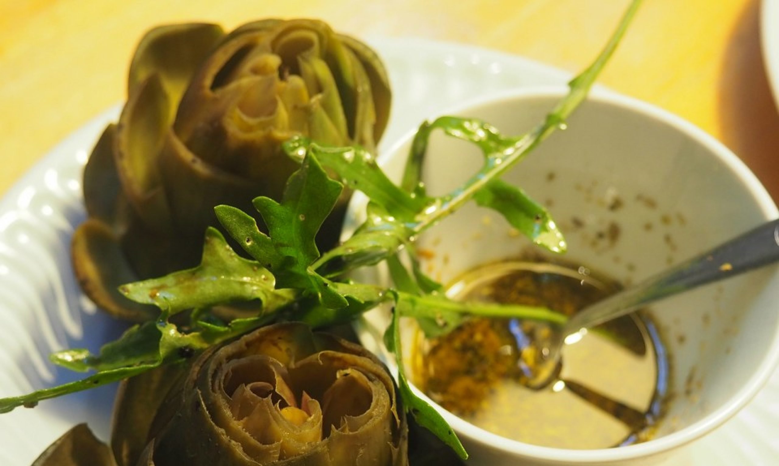 Alcachofas al vapor aderezadas con rúcula, servidas en un plato blanco con un cuenco de salsa para mojar