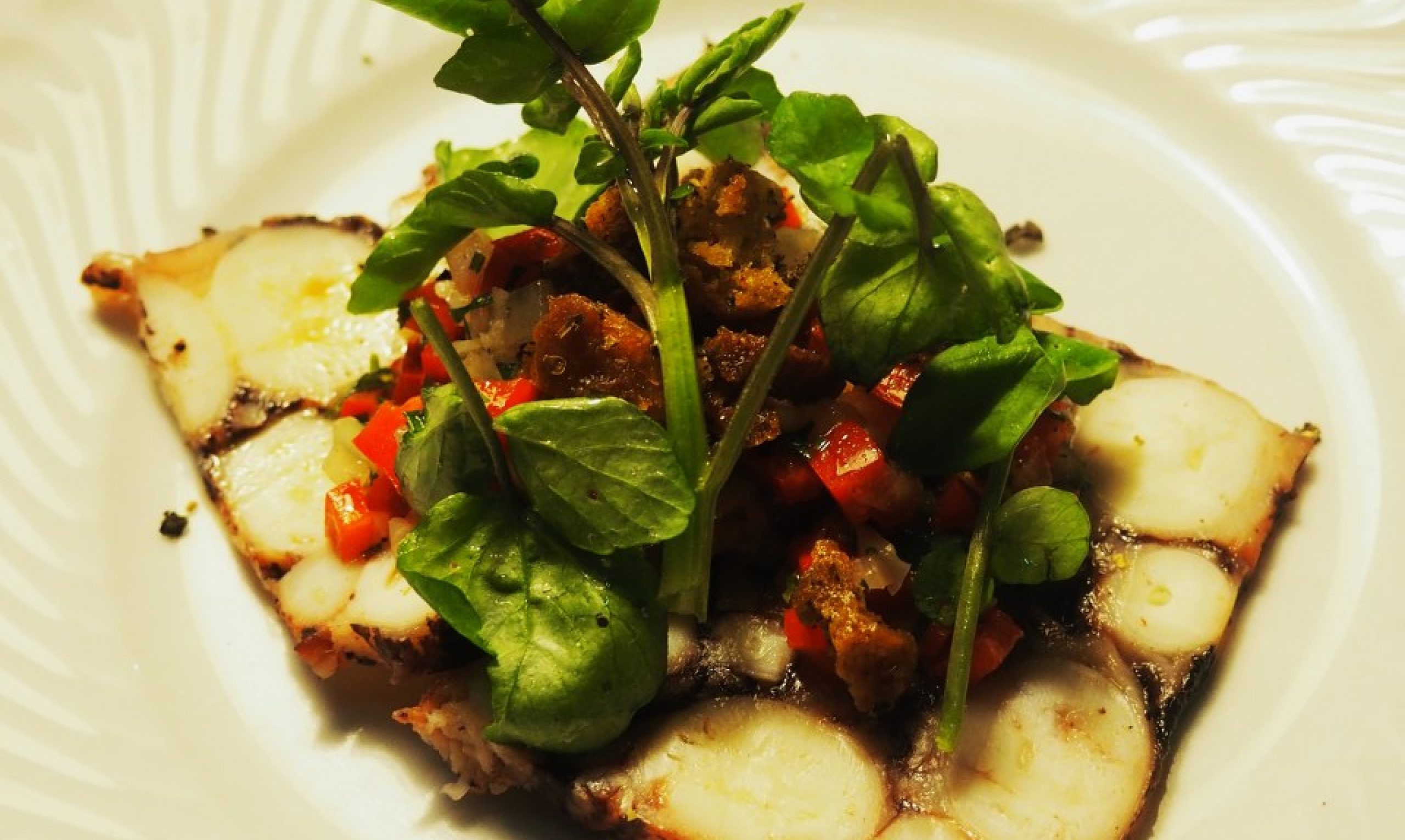 Filete de pescado a la plancha con pimientos rojos cortados en dados, picatostes y berros frescos, servido en un plato blanco