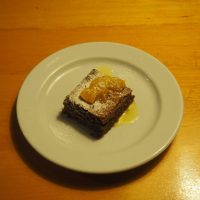Brownie de chocolate polvilhado com açúcar em pó, coberto com gomos de citrinos e calda, servido num prato branco